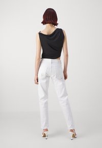 Černý dresový top s překládaným efektem spárovaný s bílými džínami s vysokým pasem. Oblečení má elegantní design a minimální zdobení.