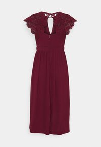 Robe bourgogne avec des manches en dentelle à volants et un dos en forme de clé, présentant une taille cintrée et une jupe fluide. Fabriquée en tissu doux.