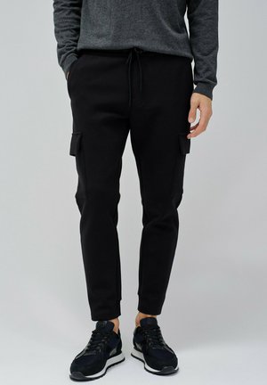 Pantalones cargo negros con bolsillos laterales, cintura elástica y puños ajustados, confeccionados en material suave. Combinados con zapatillas deportivas negras.
