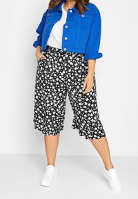 Zkrácená modrá džínsová bunda, bílý tričko a černé culottes s květinovým potiskem a bílými květy. V kombinaci s bílými teniskami.