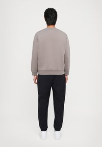 Felpa grigia con collo rotondo e maniche lunghe, abbinata a pantaloni sportivi neri a gamba affusolata e sneakers bianche. Tessuto morbido e vestibilità casual.