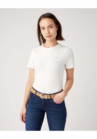 Witte katoenen t-shirt met korte mouwen, voorzien van een klein merkelogo op de linkerkant van de borst. Gecombineerd met donkerblauwe denim jeans en een tan-belt.