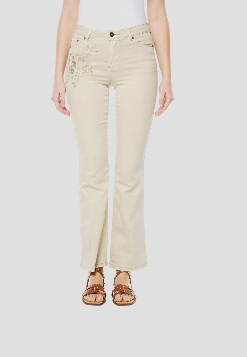 Beige ausgestellte Jeans mit floraler Stickerei auf der linken Seite, mit Vordertaschen, Knopfverschluss und glatter Stoffstruktur.