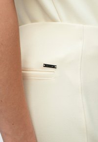 Παντελόνια Calvin Klein σε εκρού χρώμα με κομψό σχέδιο, που διαθέτουν μια μικρή μαύρη ετικέτα με το λογότυπο και υφή υφάσματος κοντά στην τσέπη.