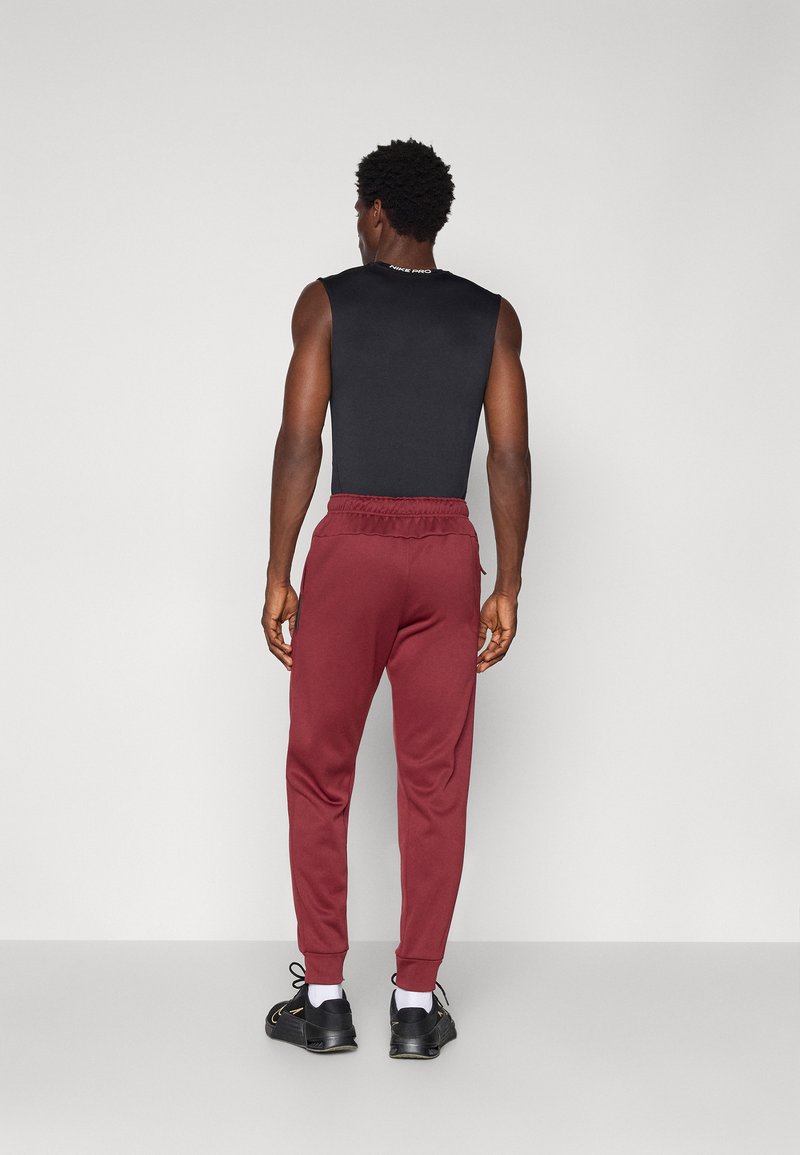 Top nero senza maniche con scollatura rotonda; pantaloni joggers bordeaux affusolati con vita elasticizzata e polsini; calzature casual nere visibili.