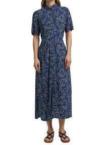 Robe midi bleu à fleurs avec manches courtes, col à revers et taille cintrée. Tissu léger à texture fluide. Portée avec des sandales marron.
