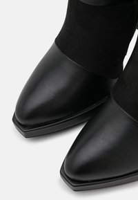 Stivaletti neri presentano una punta in pelle liscia e pannelli in camoscio. Il design include una punta affusolata e un tacco quadrato piatto.