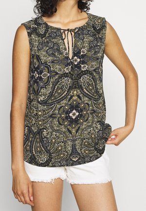 Mouwloos top met zwart, groen en beige paisley- en bloemenpatroon, strikkoordje bij de hals, gedragen met witte shorts met rafelige zoom.