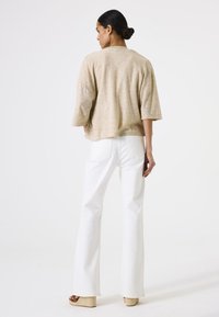 Hellbeige strukturierte Bluse mit lockerer Passform und Dreiviertelärmeln, kombiniert mit hochgeschnittenen weißen Schlagjeans und Keilsandalen.