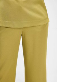 Gros plan sur un pantalon en tissu vert olive lisse avec un détail assorti au niveau de l'ourlet supérieur, montrant la taille et la partie supérieure de la cuisse.