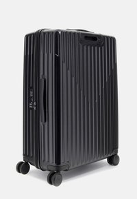 Valise rigide noire avec texture à rainures verticales, poignée rétractable, roues doubles et fermeture éclair. Design compact et durable.