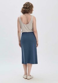 Beiger ärmelloser Top und dunkelblaue Strick-Midifalte, glatte Textur, tailliert, lässiges Design, kombiniert mit hellen Schuhen.