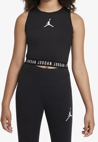 Czarny sportowy top z krótkim rękawem z białym logo Jordana, o dopasowanym kroju i stylu z wycięciem na plecach. Noszony z pasującymi czarnymi legginsami.