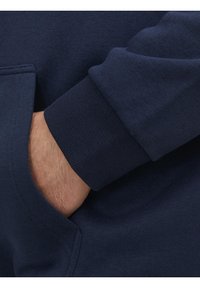 Felpa blu navy con polsini a costine e tasca a marsupio. Il materiale sembra morbido e strutturato, presentando una vestibilità comoda.