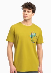 Korte mouwen, olijfgroen katoenen T-shirt met een kleurrijke grafische afdruk van een figuur en abstracte vormen op de voorkant.