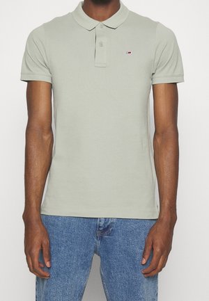 Polo shirt vert clair en coton, doté d'un col classique, d'une patte de boutonnage à deux boutons et d'un petit logo sur la poitrine. Porté avec un jeans bleu.