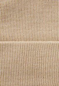 Tissu tricoté beige à texture côtelée. Le motif présente des lignes verticales espacées uniformément, créant une apparence structurée.