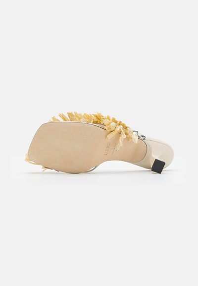 Heeled sandal with a beige leather base, adorned with yellow fringes, featuring a block heel and smooth, flat sole. Floral patterns on accents.