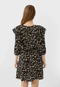Robe noire avec motif floral crème et jaune. Manches bouffantes et ceinture à la taille. Tissu léger, longueur au genou.