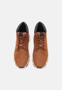 Bruine suède schoenen met zwarte accenten, voorzien van ronde veters, rubberen zool en een gewatteerde kraag voor comfort. Bovenaanzicht laat het ontwerp en de kleur zien.