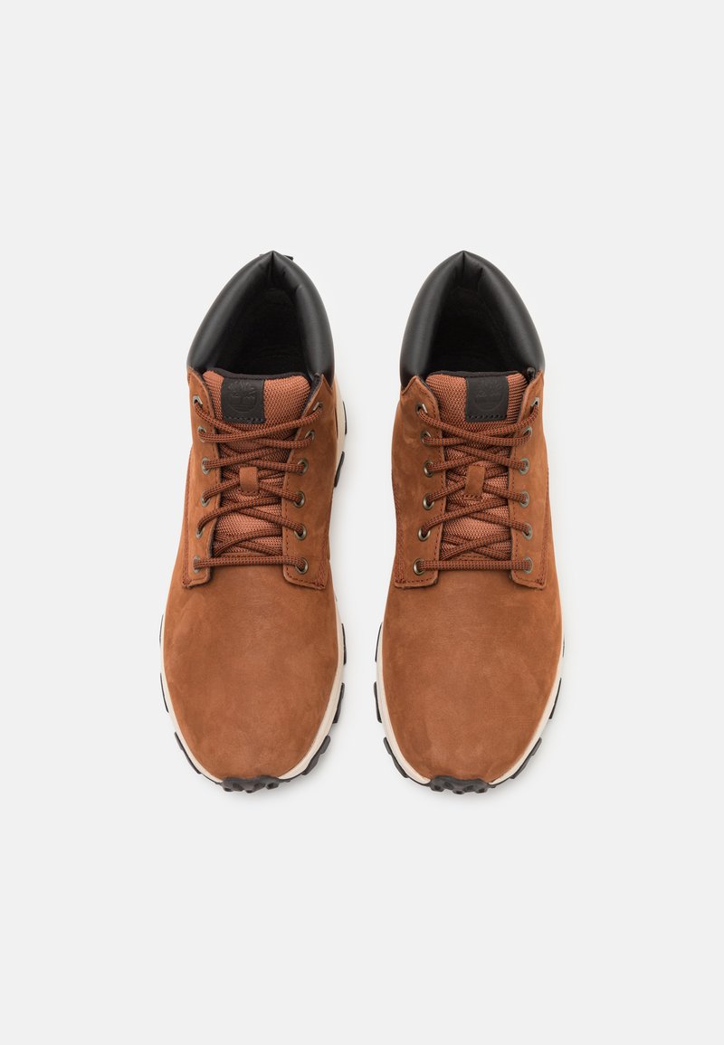 Chaussures en daim marron avec des accents noirs, dotées de lacets ronds, d'une semelle en caoutchouc et d'un col rembourré pour le confort. La vue de dessus met en valeur le design et la couleur.