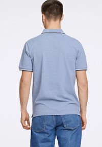 Lyseblå polo med tekstureret stof, korte ærmer og mørk trim langs kraven og ærmerne, parret med blå denimshorts.