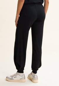 Pantalons de jogging noirs en tissu doux avec une coupe slim, dotés d'une taille élastique et de poignets élastiques. Accompagnés de baskets à accents argentés.