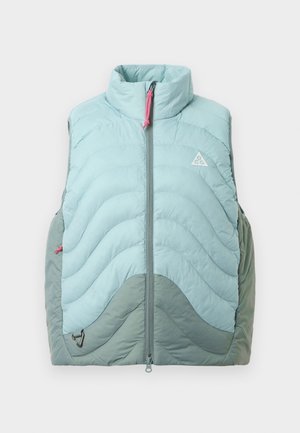 Gaiši zilas bezpiedurkņu pūšanas veste ar augstu apkakli, quilted tekstūru un izliektiem pelēkiem akcentiem, ar priekšējo rāvējslēdzēju un rozā vilkšanas cilpiņu.