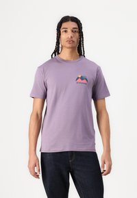 T-shirt en coton violet à manches courtes et col ras du cou, avec un graphique coloré de montagne et de soleil sur le côté gauche de la poitrine.