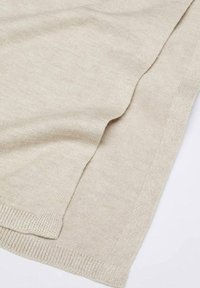 Tissu beige tricoté plié pour montrer la texture, les bords et le détail de l'ourlet côtelé sur une surface plane.