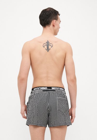 Pantaloni scurți de baie în carouri alb-negru, cu un talie elastică Moschino, prevăzuți cu buzunare laterale și o croială lejeră.