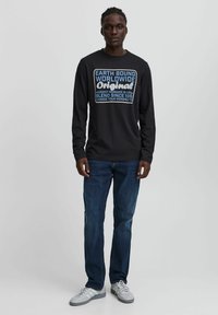 Svart langermet skjorte med stor trykt tekst i hvitt og blått. Kombinert med denimjeans og grå sneakers. Enkelt design, uformell slitasje.