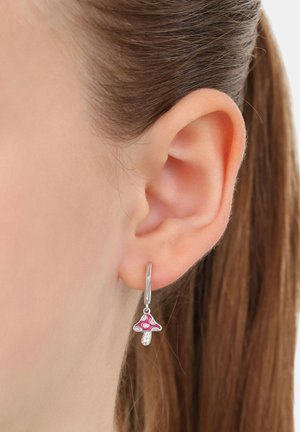 Orecchio con un orecchino ad arco d'argento che presenta un piccolo charm a forma di funghetto rosa, con i capelli castani raccolti dietro l'orecchio.