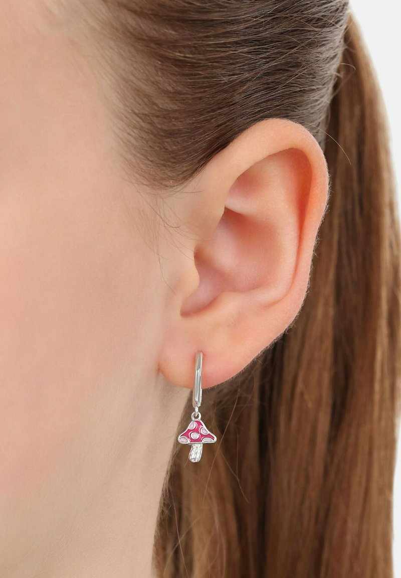 Orecchio con un orecchino ad arco d'argento che presenta un piccolo charm a forma di funghetto rosa, con i capelli castani raccolti dietro l'orecchio.