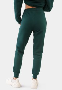 Grüne Jogginghosen aus weichem Stoff mit elastischem Bund, gerippten Knöcheln und seitlichen Taschen. Kombiniert mit weißen Sportschuhen.