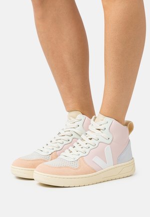 High-top sneakers in pastel pink, beige, and white with white laces, worn on bare legs against a plain background.