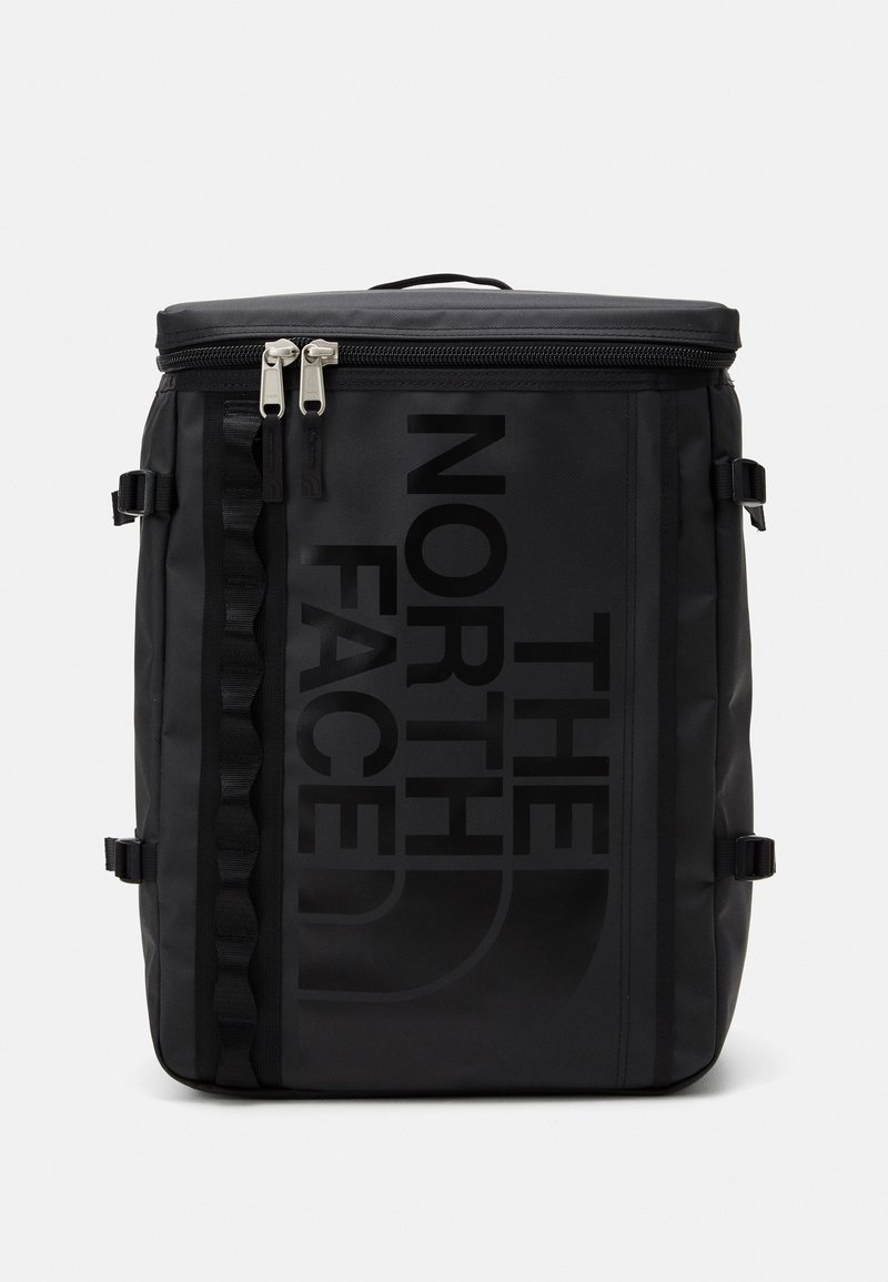 Sac à dos rectangulaire noir North Face avec logo vertical, double fermeture éclair sur le dessus et sangles de compression latérales sur fond uni.
