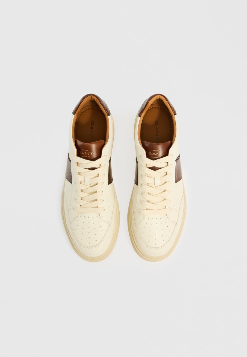 Cremfarbige Leder-Sneaker mit braunen Akzenten. Zu den Merkmalen gehören eine perforierte Zehenpartie, flache Schnürsenkel und ein hellbraunes Innenfutter. Robuste Gummisohle.