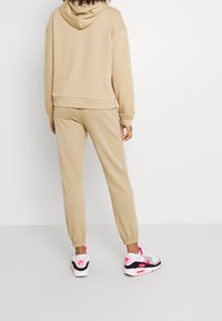 Beige hooded sweatshirt och matchande joggers, blandning av bomull, med ribbade manschetter och en avslappnad passform. Sneakers med rosa inslag och svarta detaljer.