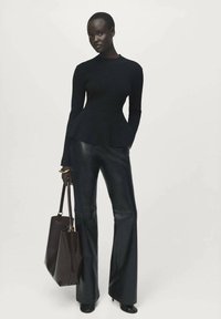 Maglia nera a coste con maniche lunghe e orlo a campana, abbinata a pantaloni in pelle nera a vita alta e a zampa; modella che tiene una borsa a tracolla marrone.