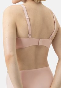 Soutien-gorge rose clair avec bretelles réglables et finition lisse. Il dispose d'une fermeture à crochets à l'arrière et d'un design sans coutures.