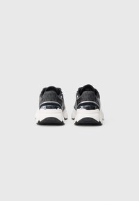 Une paire de baskets noires et grises avec des semelles blanches et des accents réfléchissants argentés au niveau du talon, montrée de dos sur un fond blanc.