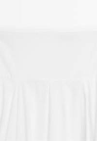 Robe blanche épaules dénudées avec un corsage ajusté et un tissu fluide sous la couture de la poitrine, présentée sur un fond blanc uni.