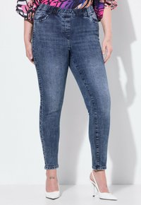 Wąskie dżinsy w ciemnoniebieskim deninie, z wysokim stanem, lekkim przetarciem i metalowymi ćwiekami wzdłuż bocznych szwów.