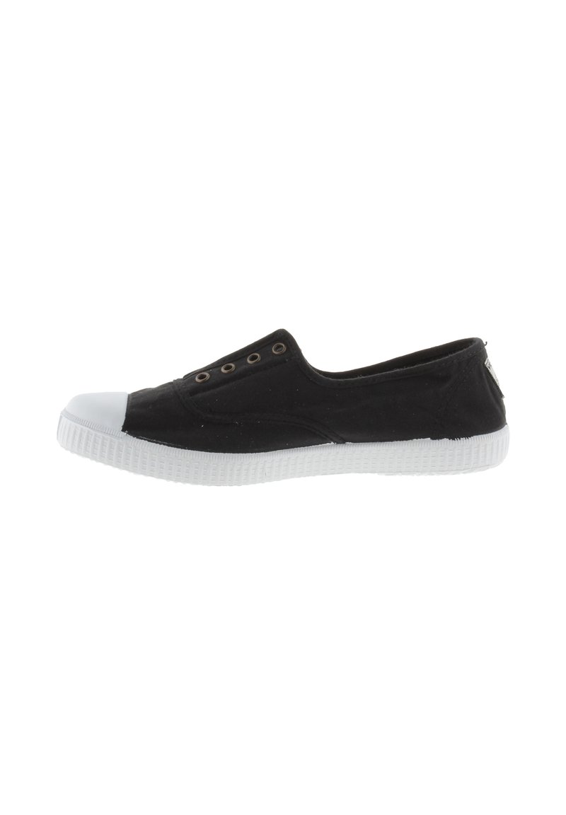 Zapato de tela negro sin cordones con puntera y suela de goma blanca. Presenta ojales metálicos en la parte superior para ventilación. Diseño minimalista.
