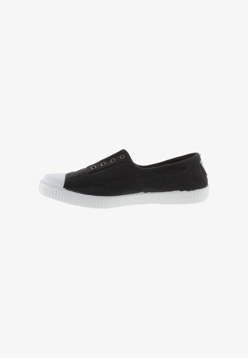 Zapato de tela negro sin cordones con puntera y suela de goma blanca. Presenta ojales metálicos en la parte superior para ventilación. Diseño minimalista.