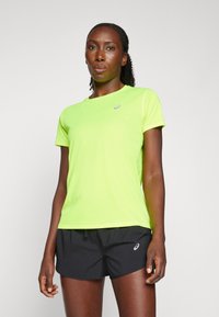 Neon sárga sportpóló kerek nyakkivágással és rövid ujjal, fekete sorttal párosítva, amelyen logó díszítés található. Sima tapintású.