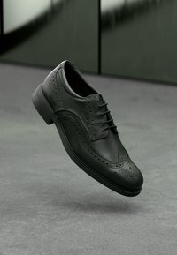 Pantofii oxford din piele neagră, cu detalii perforate, textură netedă și vârf rotund. Prezintă un sistem de închidere cu șireturi și o talpă durabilă.