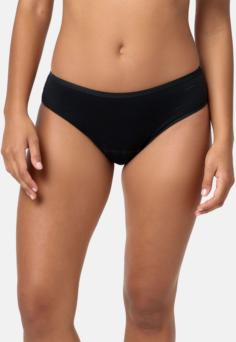 Donna che indossa un intimo stile bikini nero semplice, mostrata dalla metà del torso fino alla parte superiore delle cosce su uno sfondo chiaro.