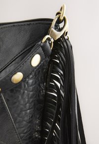 Schwarze Leder-Taschenecke mit goldenen Nieten, goldener Schnalle und langen schwarzen Lederfransen, die seitlich herabhängen.